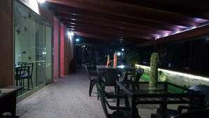 Un área de patio al aire libre con mesas y sillas, una pared de vidrio y piso de ladrillo.