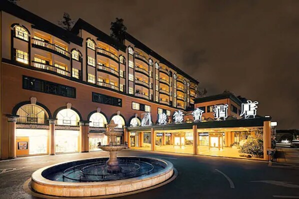 Een hotel met een fontein in de binnenplaats, meerdere verdiepingen en verlichte borden.