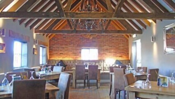 A rustic dining area with exposed wooden beams, brick walls, and multiple tables and chairs.