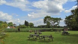 An outdoor area with picnic tables and benches, surrounded by greenery and trees.
