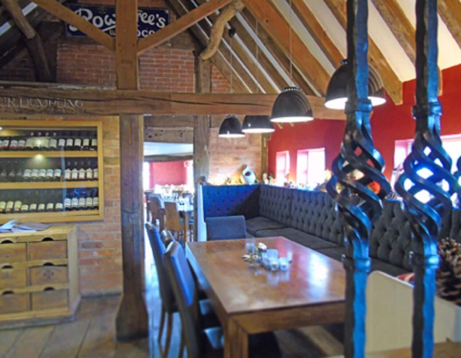 A restaurant interior with a wooden ceiling, brick walls, a blue upholstered bench, and a wooden table with chairs.