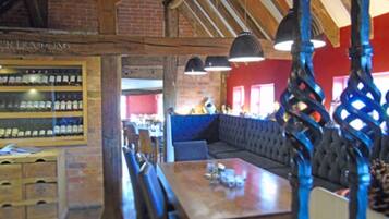 A restaurant interior with a wooden ceiling, brick walls, a blue upholstered bench, and a wooden table with chairs.