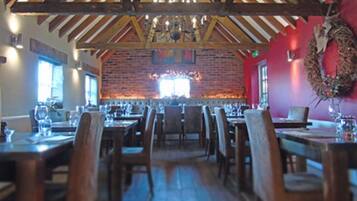 Un restaurante con mesas y sillas de madera, un muro de ladrillo y una araña.