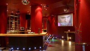 A bar area with a counter, bar stools, and a screen displaying a face. - Hotel Las Eras (Zafra)