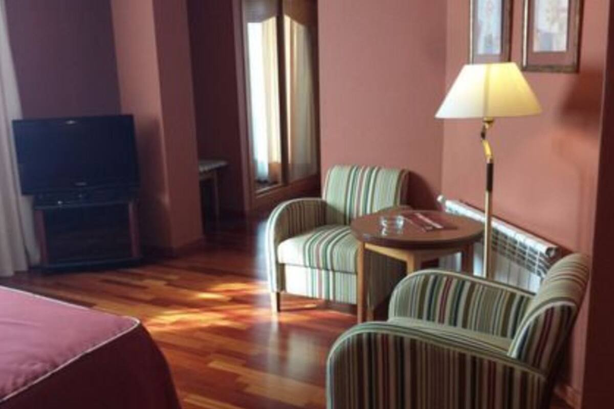 A hotel room with a bed, a television, a sofa, a chair, a table, and a lamp.