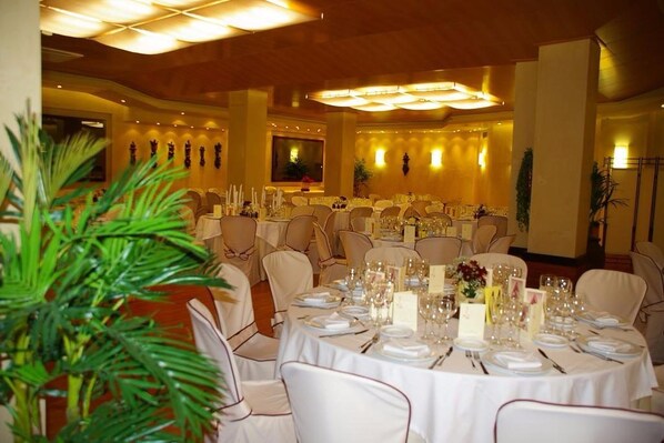 A banquet hall with round tables set for dining, surrounded by chairs.