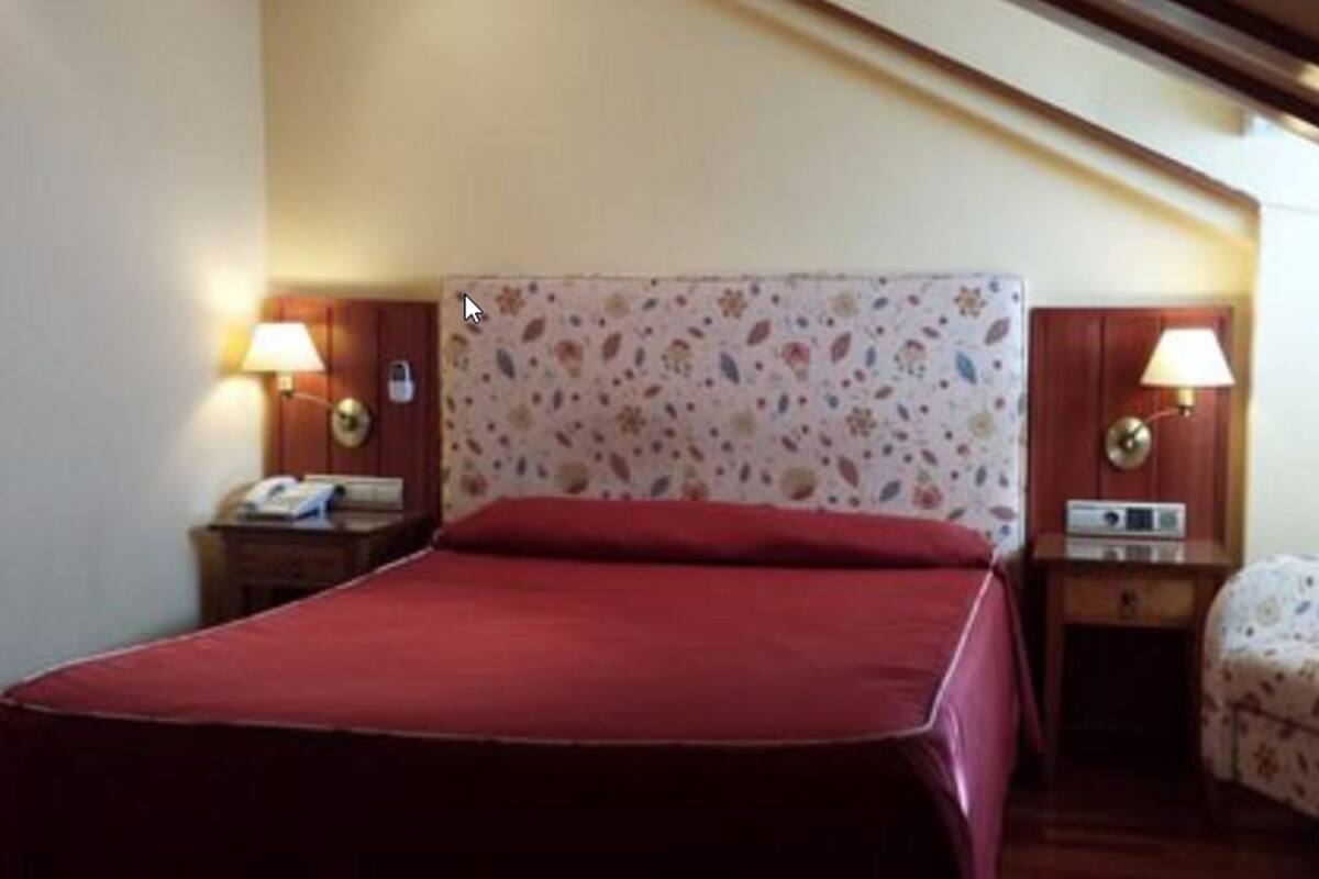 A hotel room with a bed, two bedside tables, lamps, and a small chair.