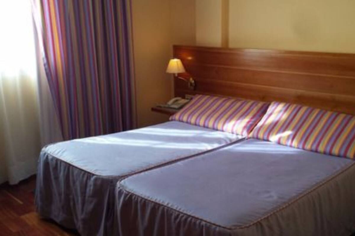 A double bed with a wooden headboard, a bedside lamp, and striped curtains.
