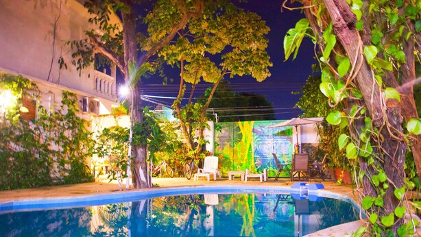 A swimming pool with a chair and a bicycle, surrounded by greenery and a building with a mural. - Nativ Tulum Hotel Boutique (Tulum)