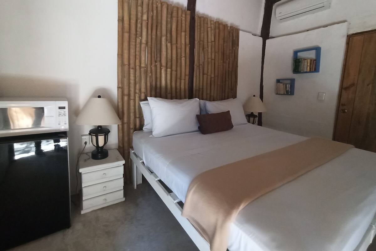Une chambre à coucher comprenant un lit, des tables de chevet, un four à micro-ondes et un climatiseur fixé au mur.