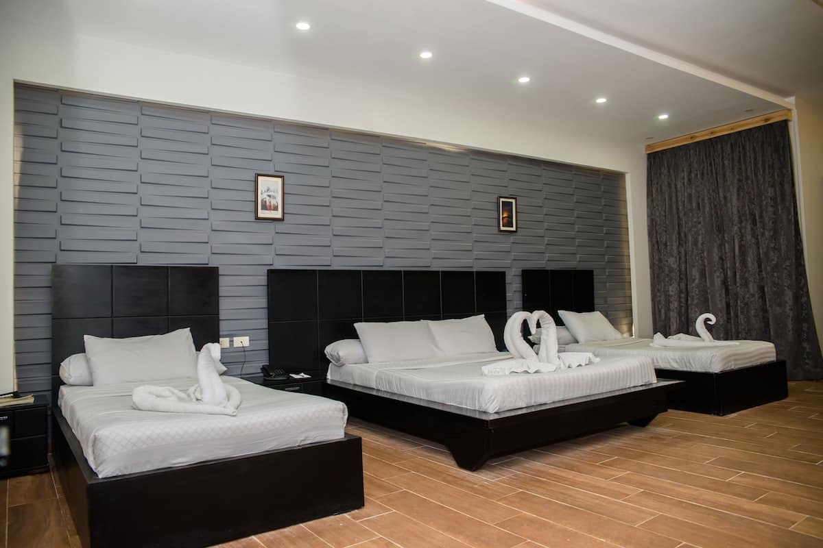 Habitación de hotel con tres camas, una pared gris con textura y un ventanal con cortinas.