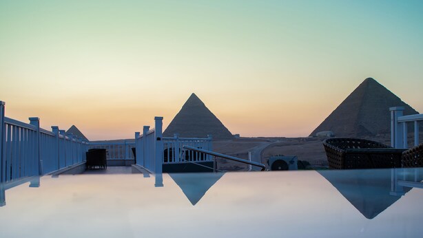A reflective pool with a view of pyramids and a white fence. - Marvel Stone Hotel (Giza)