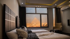 A hotel room with a large bed, a chair, and a window with a view of a pyramid. - Marvel Stone Hotel (Giza)