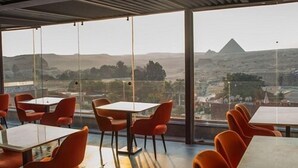 A modern dining area with tables and chairs, large windows offering a view of a mountainous landscape. - Marvel Stone Hotel (Giza)