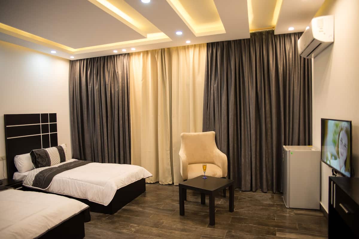 Una habitación de hotel con cama, una silla, una mesita y un equipo de aire acondicionado.