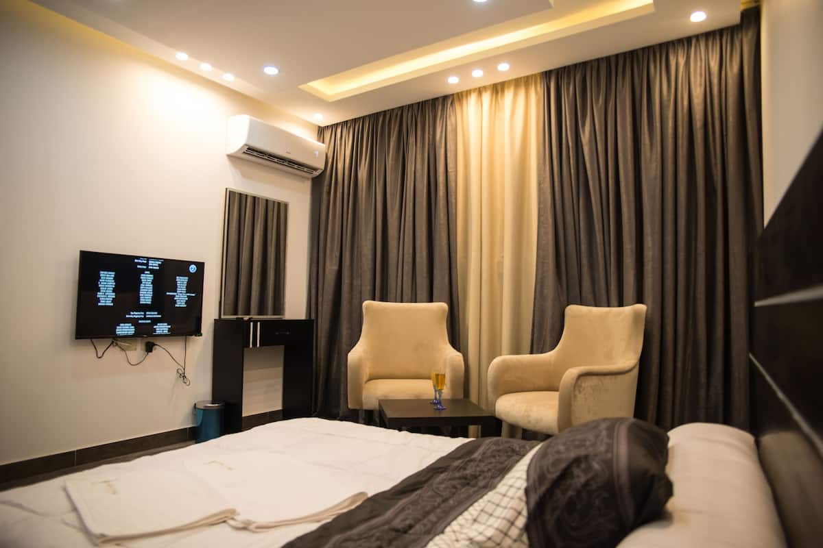 Habitación de hotel con una cama, dos sillones, una mesita, televisor montado en la pared y una ventana con cortinas.