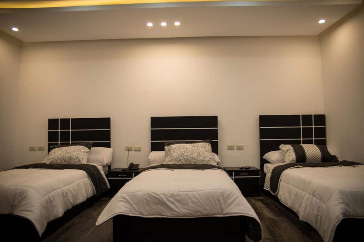 Habitación de hotel con tres camas, cada una con cabecero negro y ropa de cama blanca.