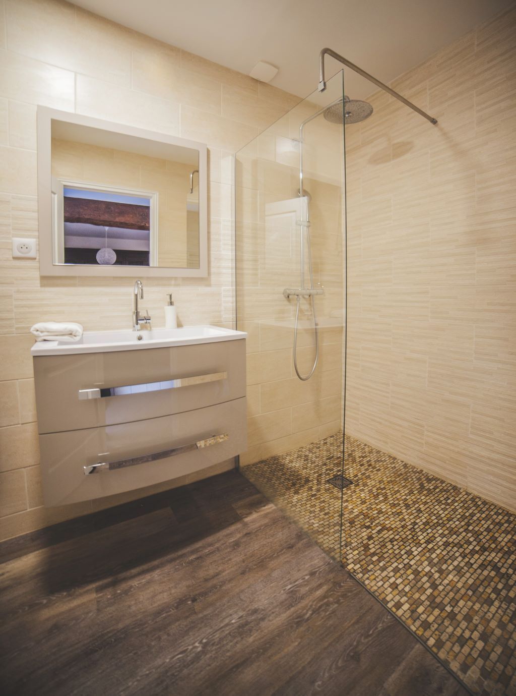 Un baño moderno con ducha de vidrio, tocador con espejo y suelo de mosaicos.