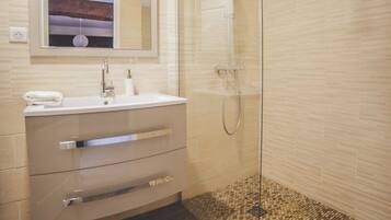 Un baño moderno con ducha de vidrio, tocador con espejo y suelo de mosaicos.