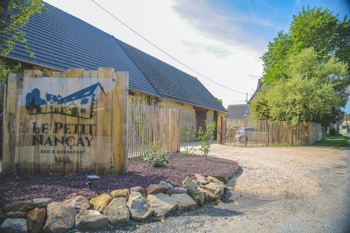A rustic bed and breakfast sign for "Le Petit Nancay" with a stone pathway leading to the entrance.