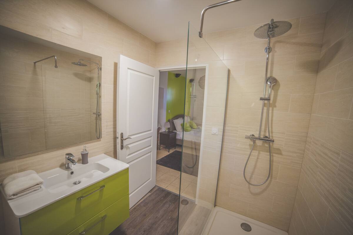 A modern bathroom with a glass-enclosed shower, a white sink, and a green vanity.