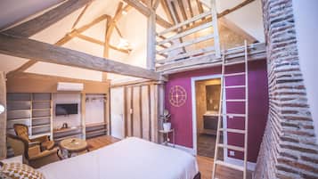A bedroom with a large bed, wooden beams, a TV, a chair, a small table, and a bathroom with a red wall and a ladder.