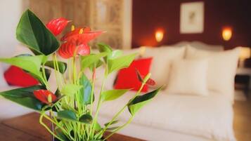 A potted plant with red flowers on a wooden table in a room with a white couch and red cushions.