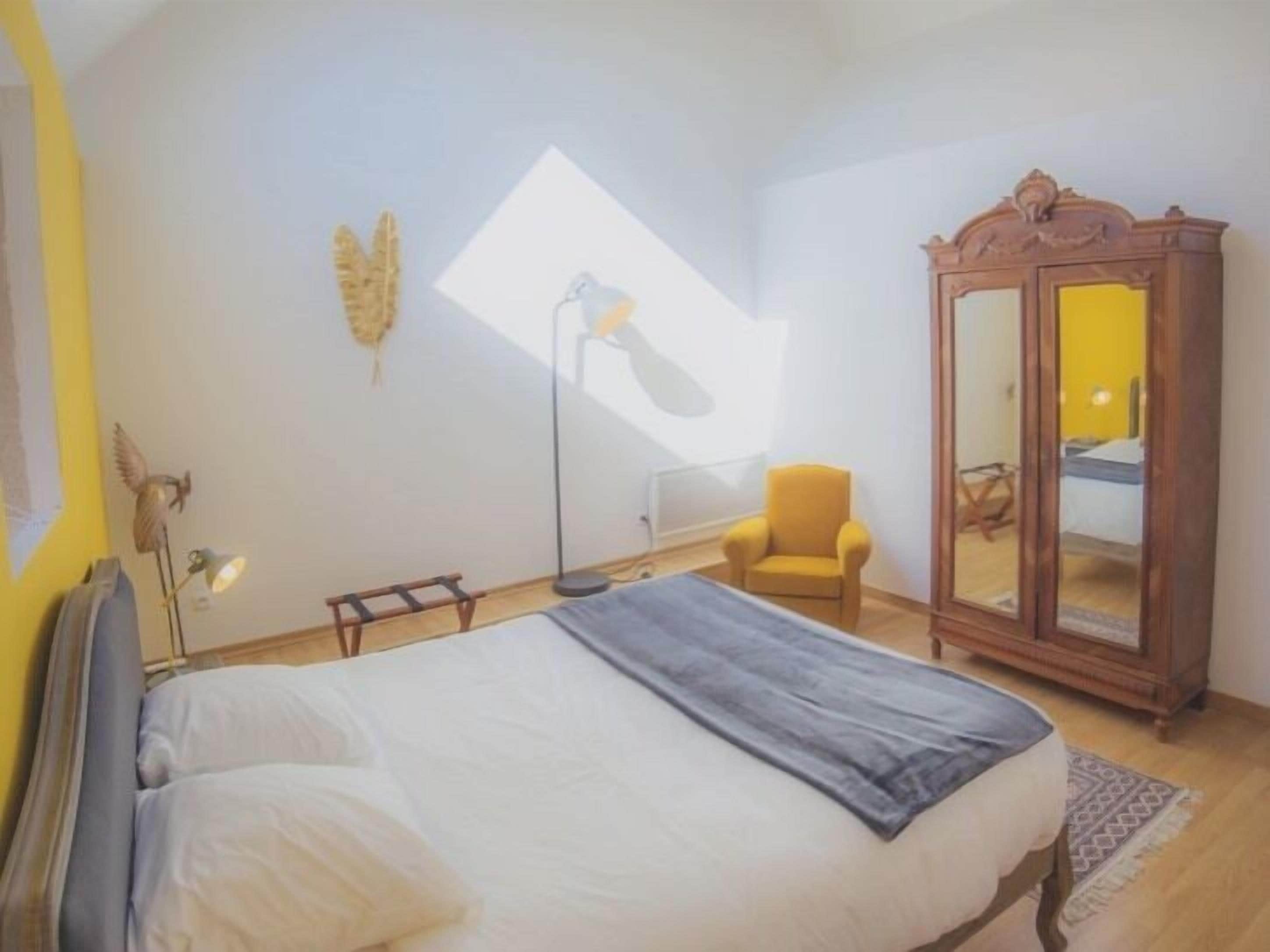 A bedroom with a bed, a chair, a wardrobe, and a floor lamp.