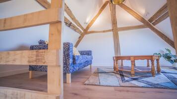 A loft bedroom with exposed wooden beams, a blue patterned sofa, a wooden table, and a potted plant.