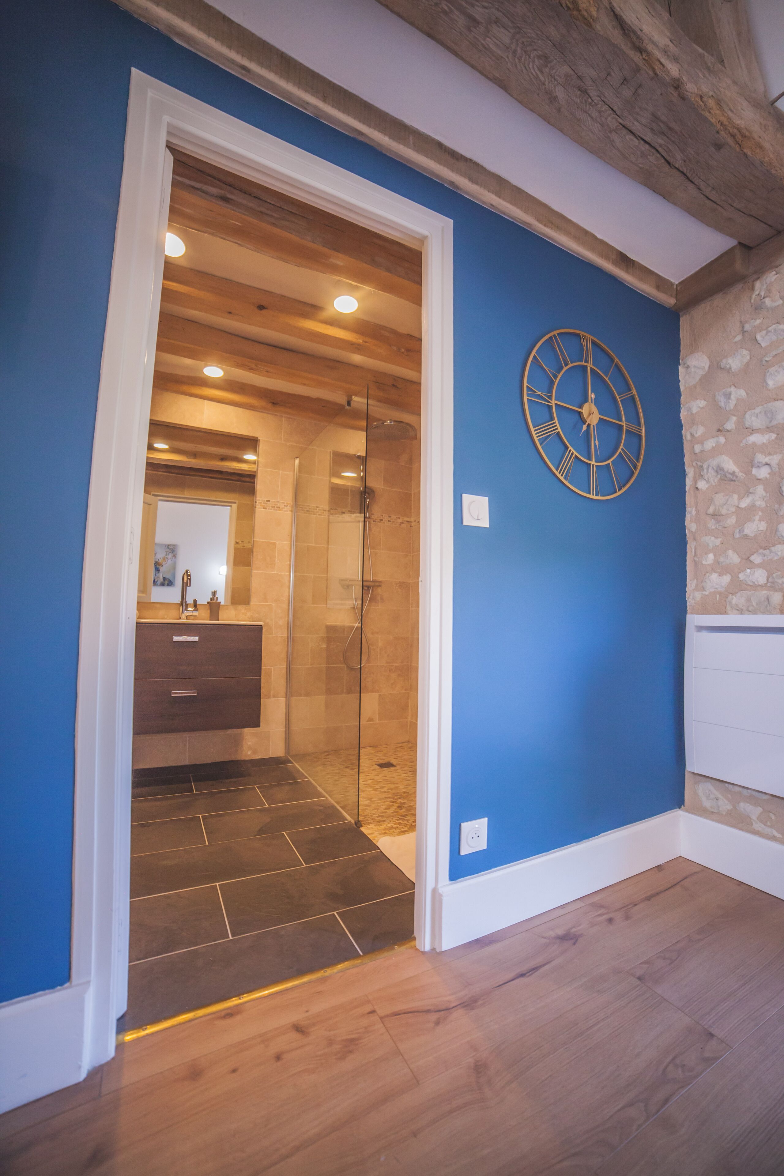 A bathroom with a glass shower, a wooden vanity, and a blue wall with a decorative clock.