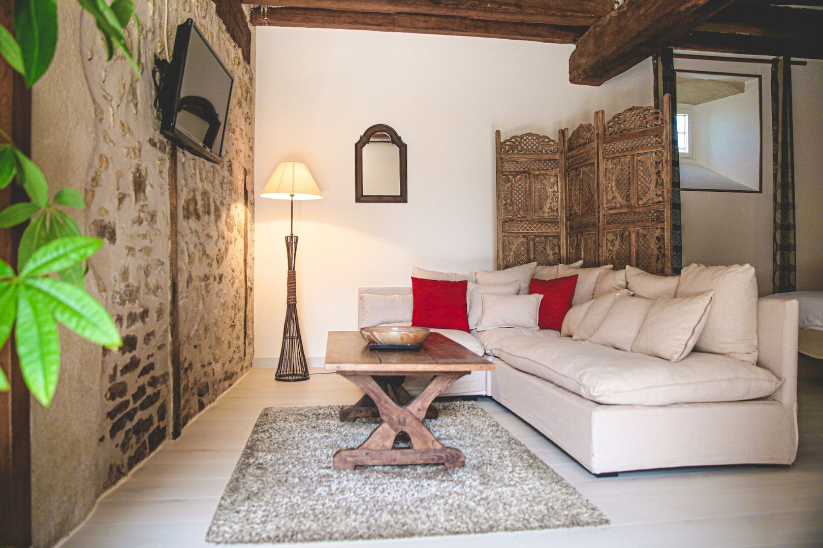 A cozy living room with a white sofa, a wooden coffee table, a lamp, and a decorative mirror.