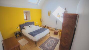 Une chambre à coucher comprenant un lit, des tables de chevet, une armoire, une lampe sur pied et une lucarne.
