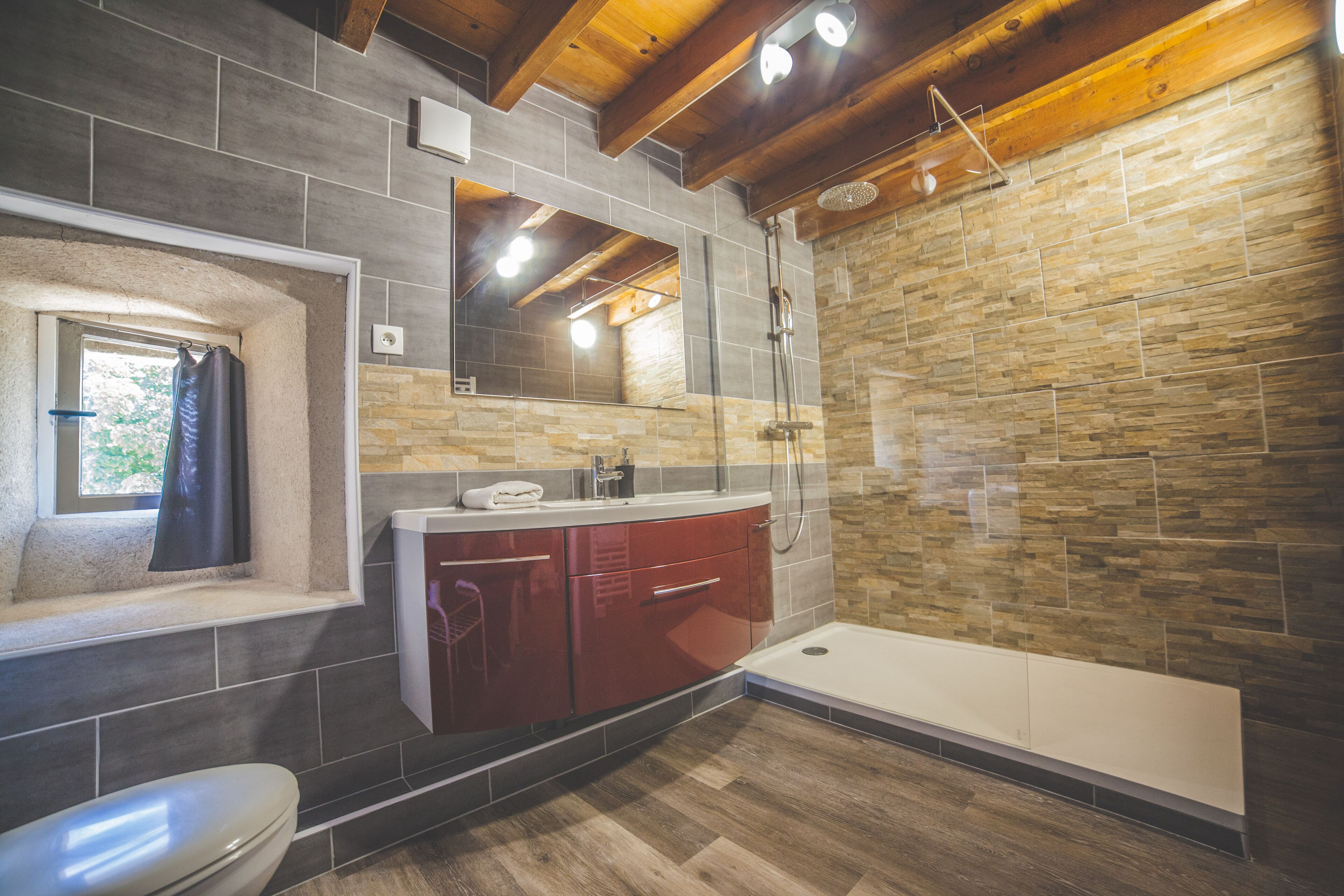 A modern bathroom with a stone wall, a wooden ceiling, a built-in sink, and a separate shower area.