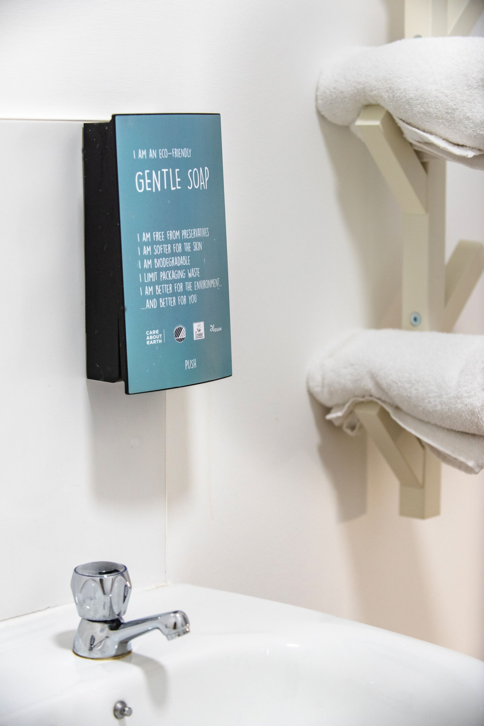 A bathroom with a sink, a towel rack, and a soap dispenser.