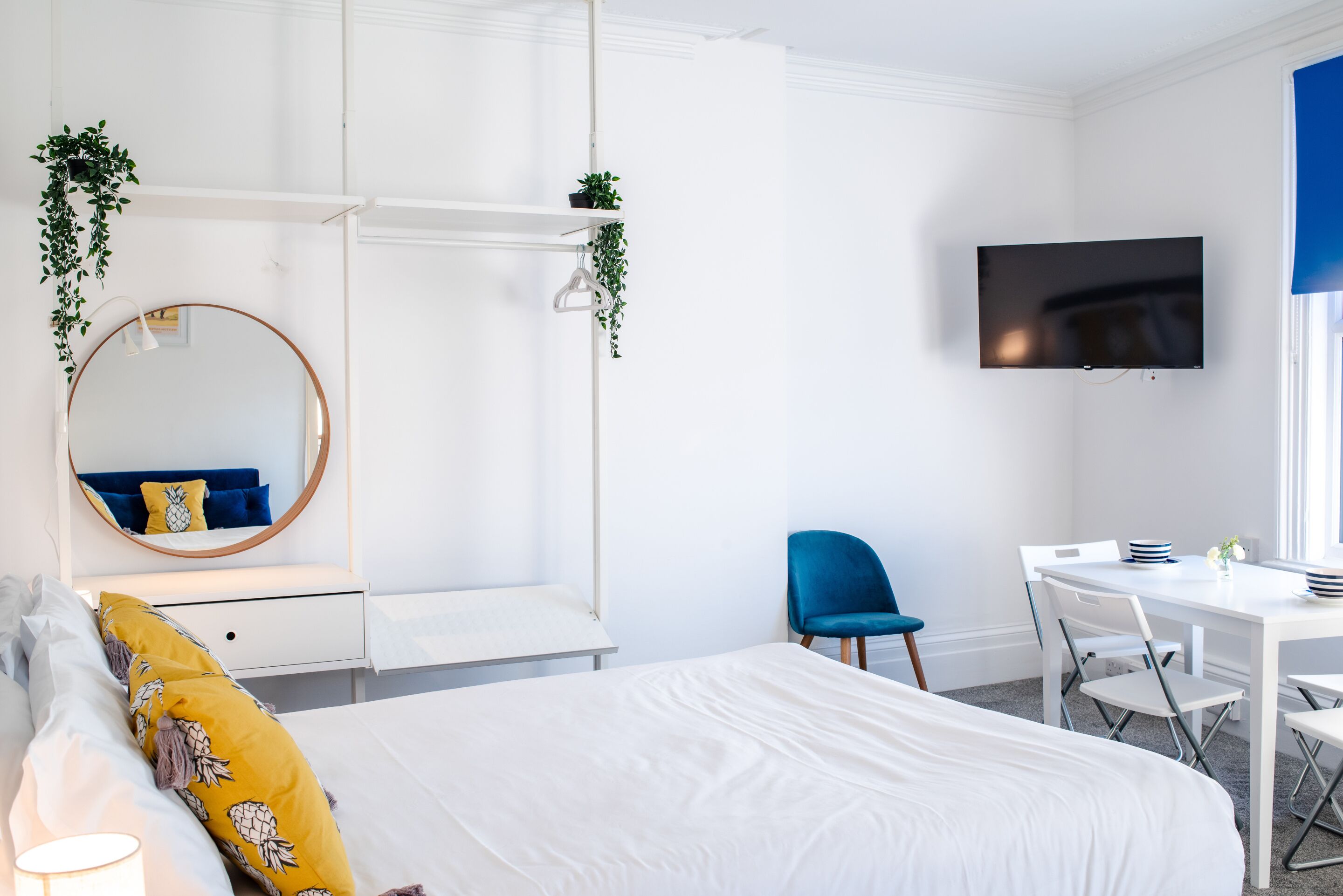 Quarto moderno com cama, escrivaninha, cadeira, televisão e espelho.