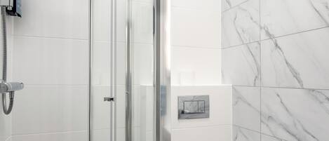 A modern bathroom with a glass-enclosed shower, a toilet, and a marble-tiled wall.