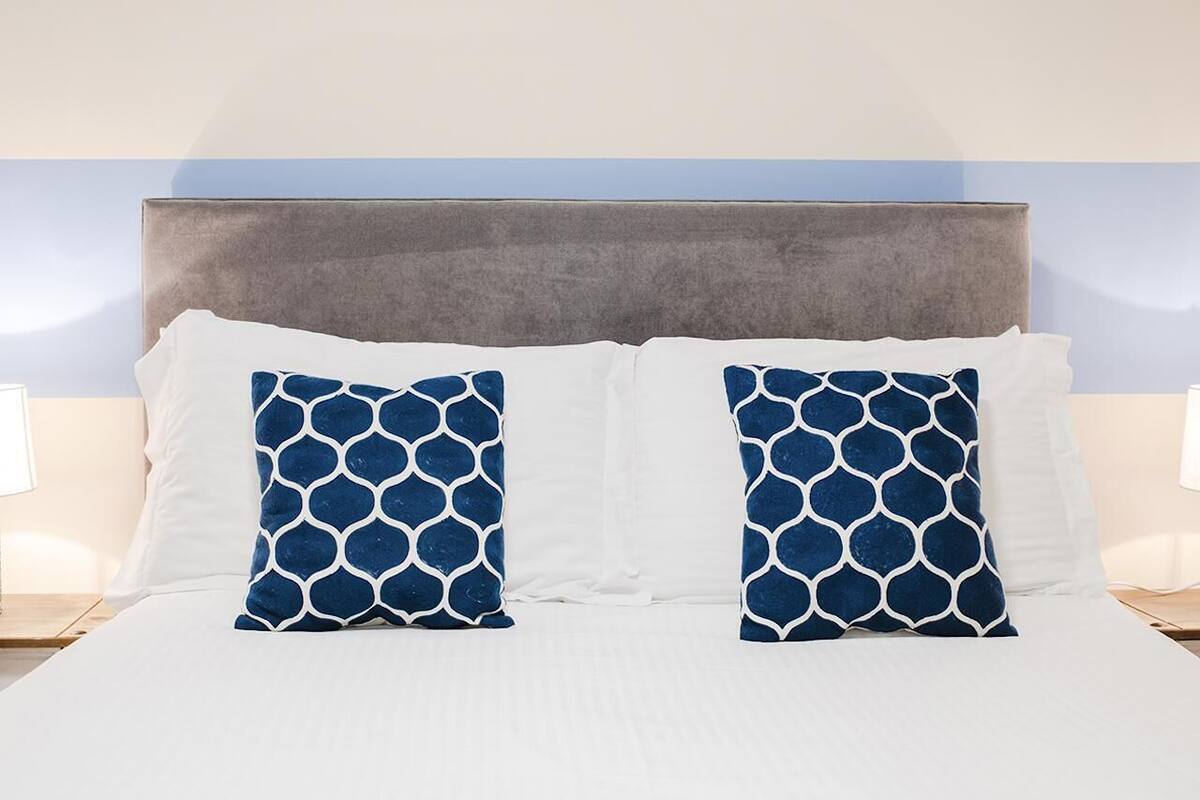 A bed with white bedding and two blue patterned pillows, a grey headboard, and bedside lamps.