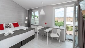 Ein modernes Hotelzimmer mit Bett, einem kleinen Tisch mit Stühlen, einem Fenster mit Stadtblick und einem Balkon.