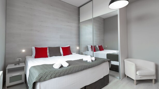 Ein modernes Hotelzimmer mit einem großen Bett, einem Nachttisch, einem Schminktisch und einem weißen Sessel.