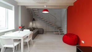 Ein modernes Interieur mit einem weißen Esstisch, einem grauen Sofa, einem roten Sitzsack und einer Wendeltreppe vor einer roten Wand.