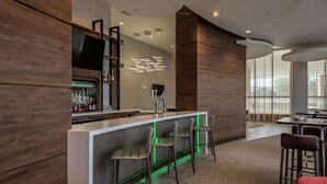 Un área de bar moderna con una barra blanca, taburetes de bar de neón verde y una variedad de botellas de licor.
