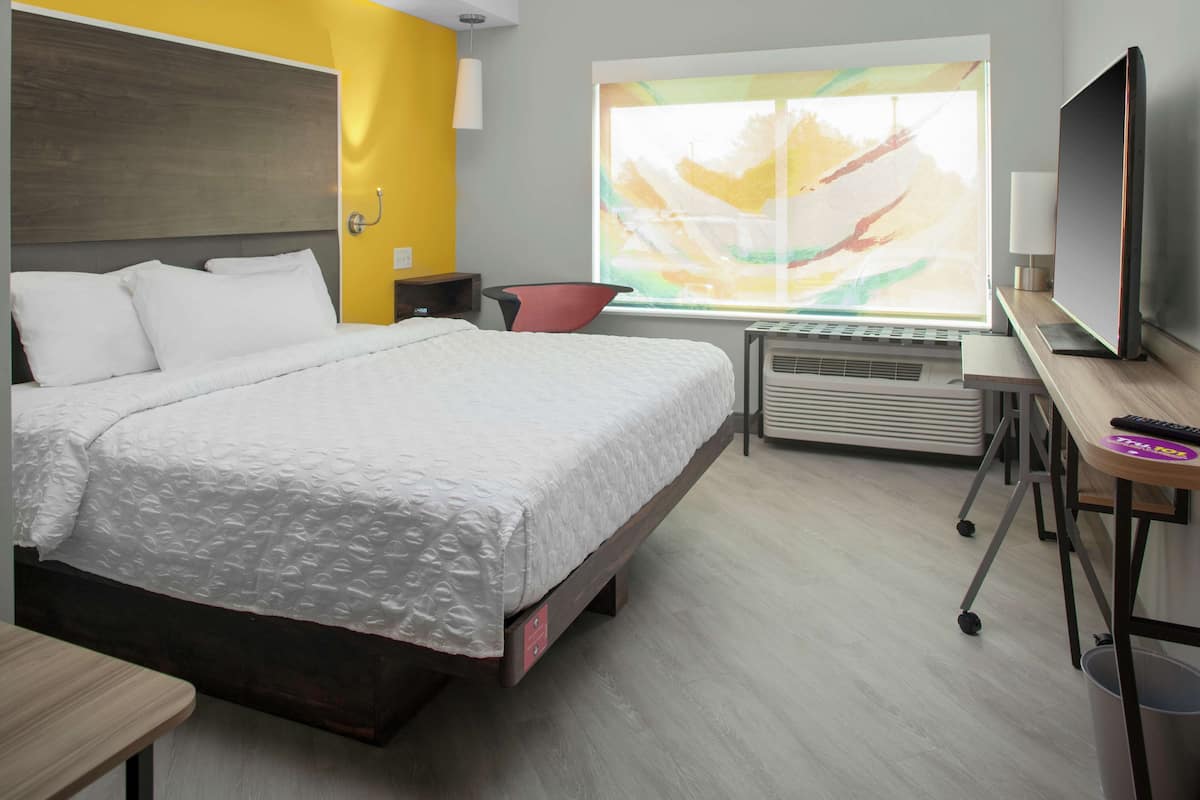 A hotel room with a bed, a desk, a chair, a TV, and a window with a view.