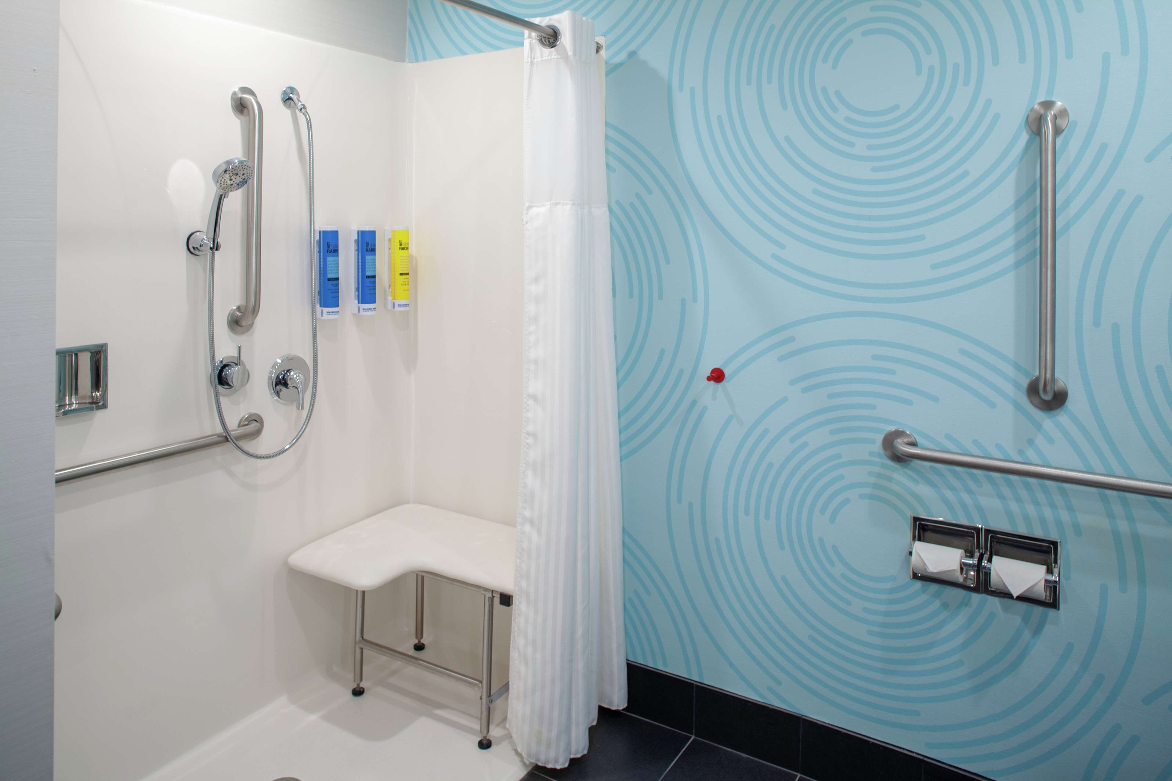 Ein Badezimmer mit Dusche, Haltegriffen, einer Sitzbank und einem Handtuchhalter.