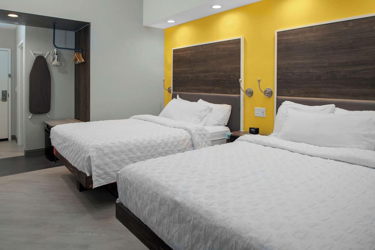 A hotel room with two beds, a wooden headboard, and a yellow accent wall.