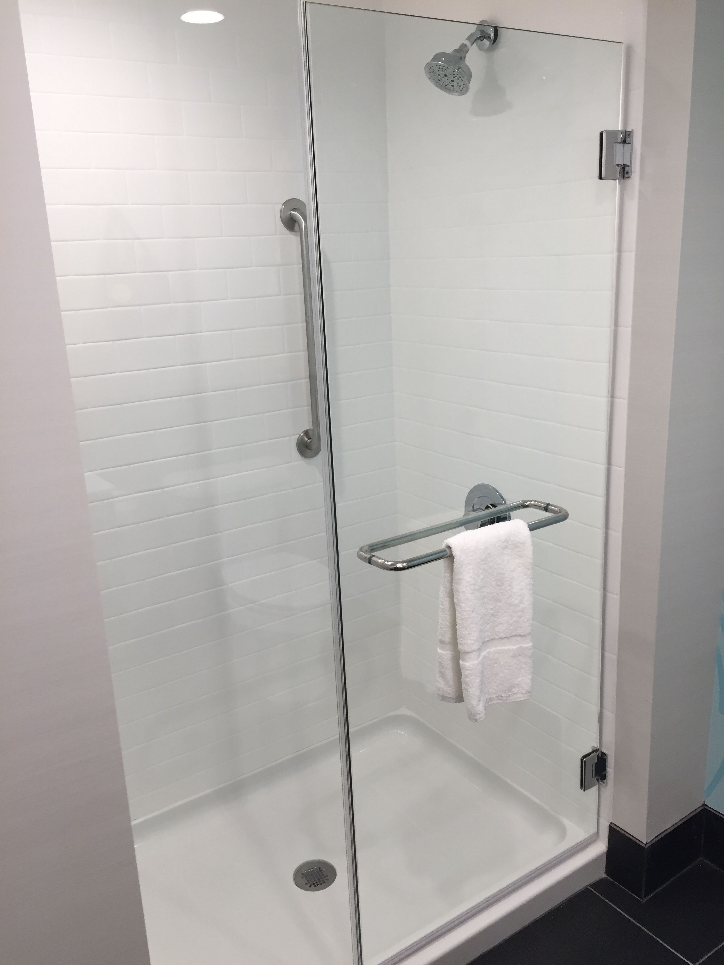 A glass-enclosed shower with a white tiled wall, a glass door, and a metal towel rack with a white towel.