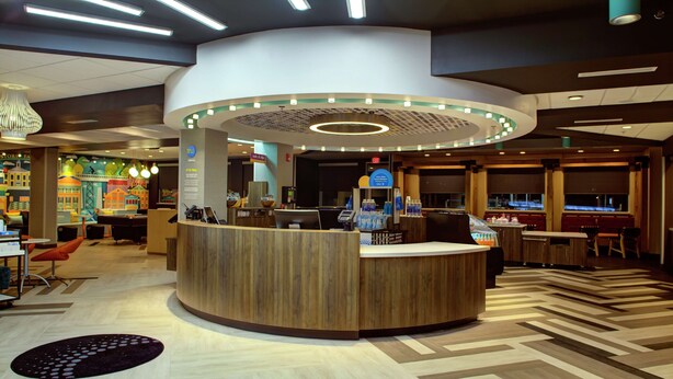 A reception area with a wooden counter, a seating area with tables and chairs, and a decorative wall with a cityscape mural. - Tru by Hilton Farmville (Farmville)