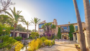 A courtyard with a pool, palm trees, and a building with a tiled roof and arched windows. - Villa Portol (Marratxi)