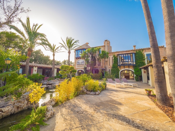 A courtyard with a pool, palm trees, and a building with a tiled roof and arched windows.