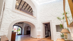 A spacious interior with white walls, a wooden floor, and a colorful rug. There are two archways leading to another room, and a balcony with a railing. - Villa Portol (Marratxi)