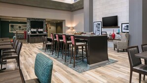 Un hall d’hôtel spacieux comprenant un bar, des espaces aménagés avec des sièges et un téléviseur fixé au mur.